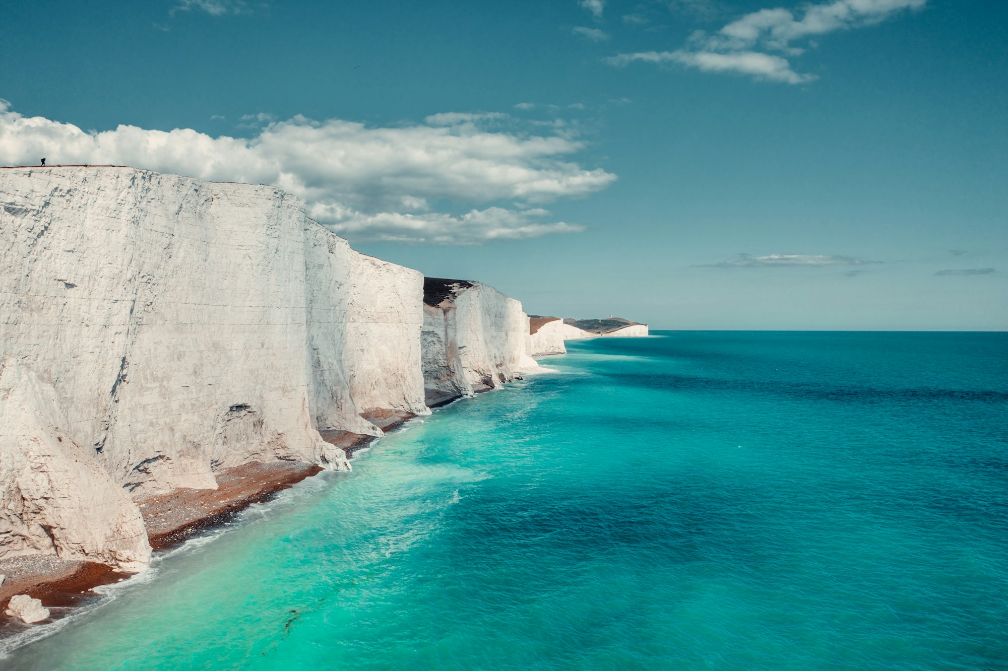 White chalk cliffs above a turquoise sea under a blue sky, on the Sussex coast